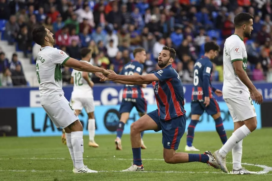 Martos, jugador del Huesca, se levanta con la ayuda de un jugador del Elche. 