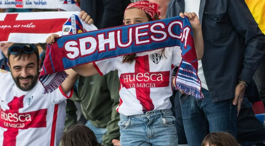 Varios aficionados del Huesca levantan sus bufandas en un partido.