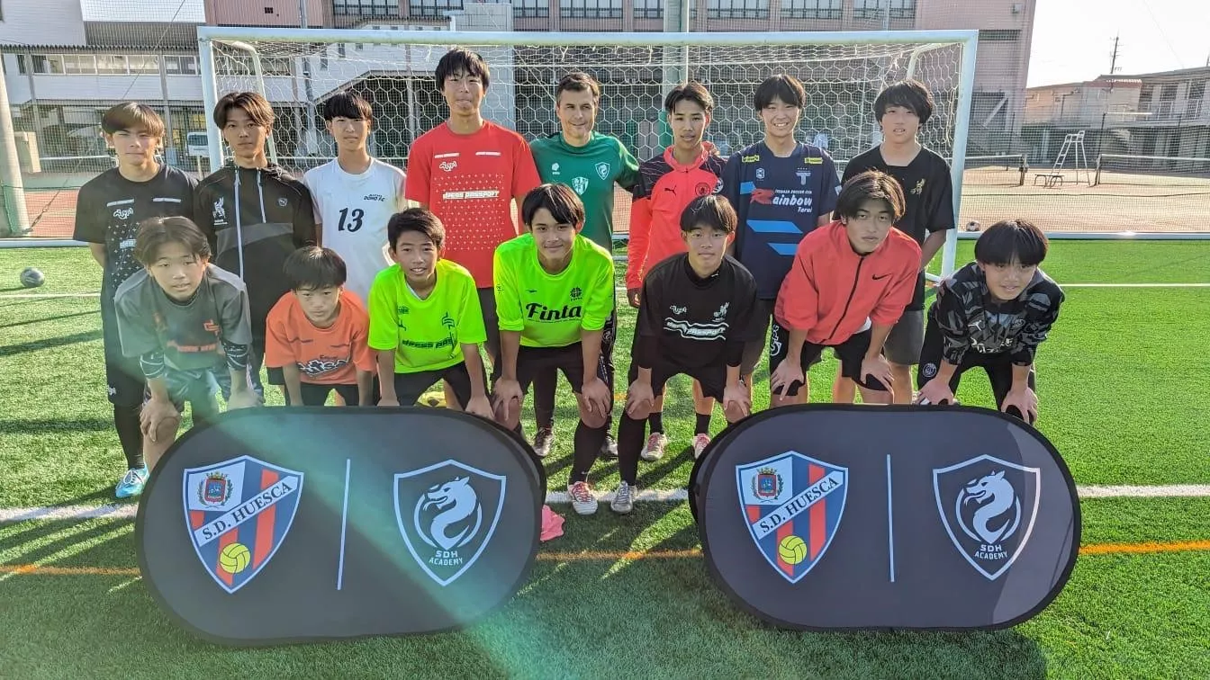 Juanjo Camacho, con japoneses y los escudos del Huesca y la SDH Academy