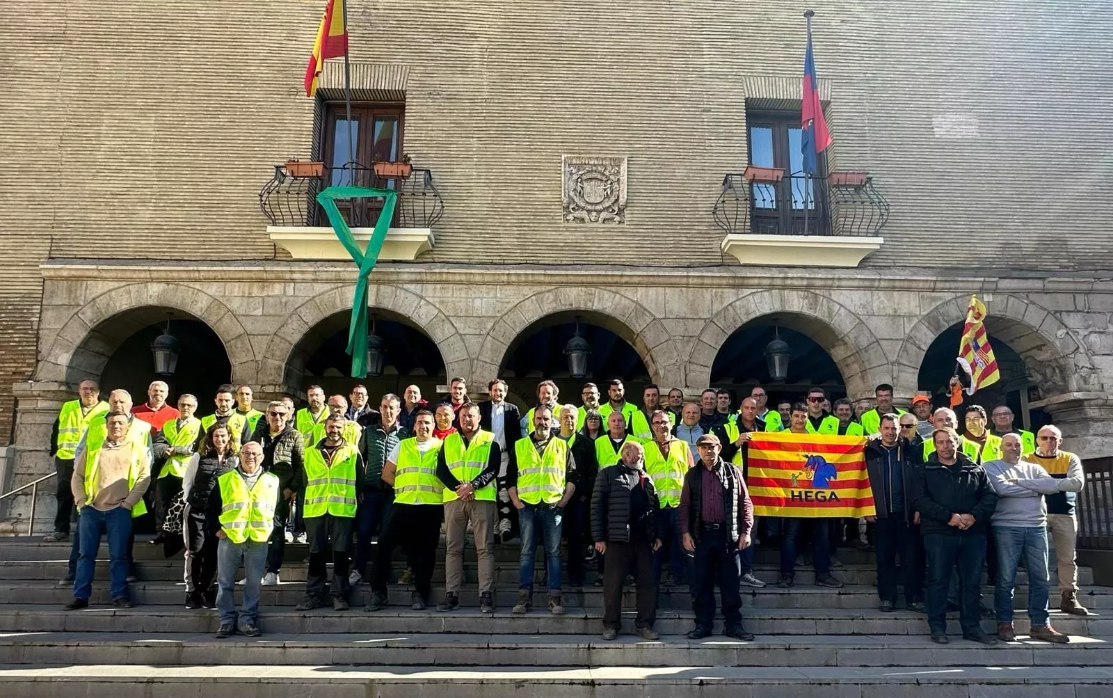 Miembros de la plataforma Hega con el alcalde de Mozón ante la fachada del Ayuntamiento, donde se ha colgado un gran lazo verde.