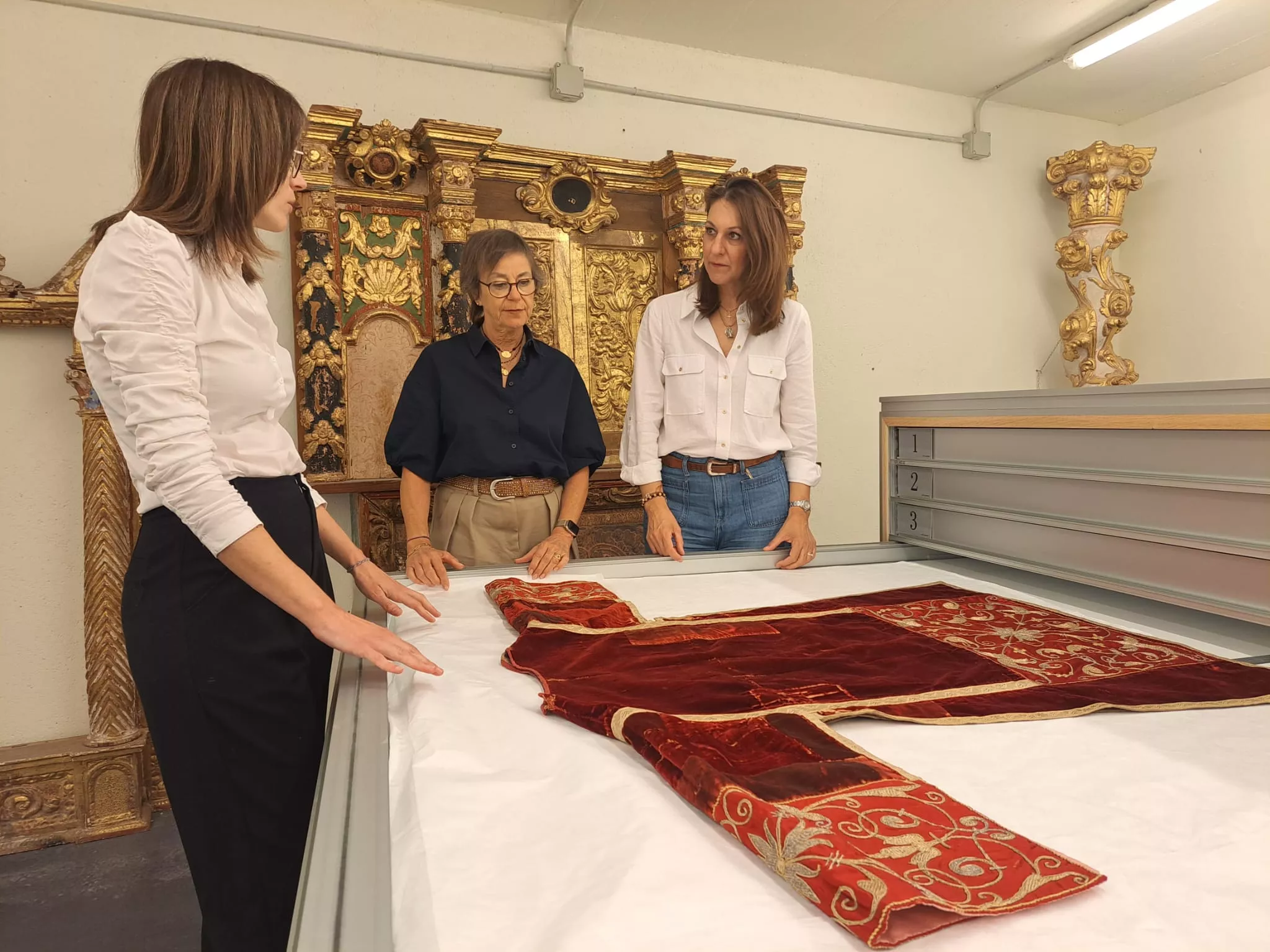 María Puértolas, Patricia Bravo y Blanca Galindo con los textiles en la cajonera que ha apoyado el Ayuntamiento