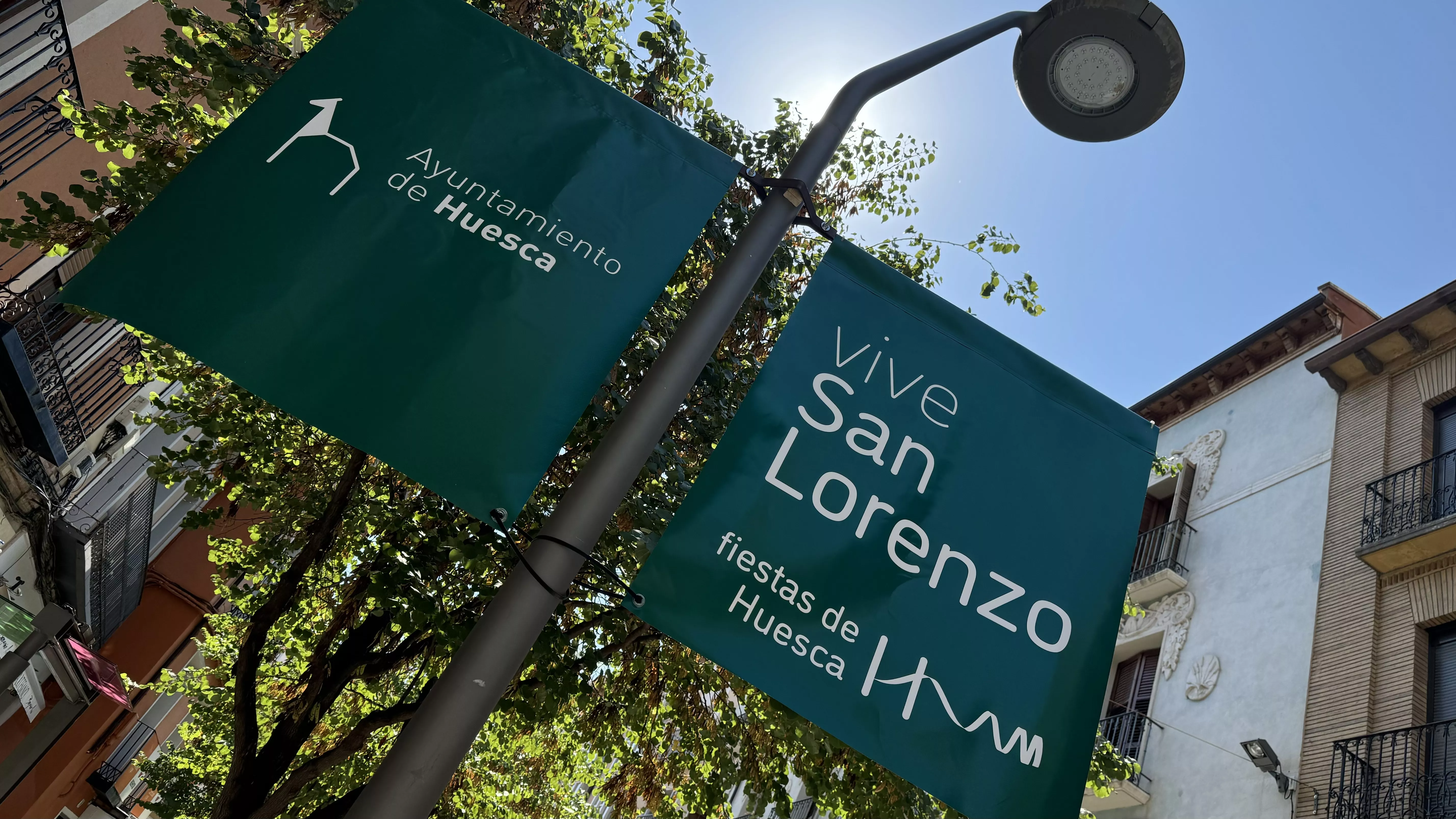 Baderolas con el lema Vive San Lorenzo instalados en 25 farolas de Huesca.