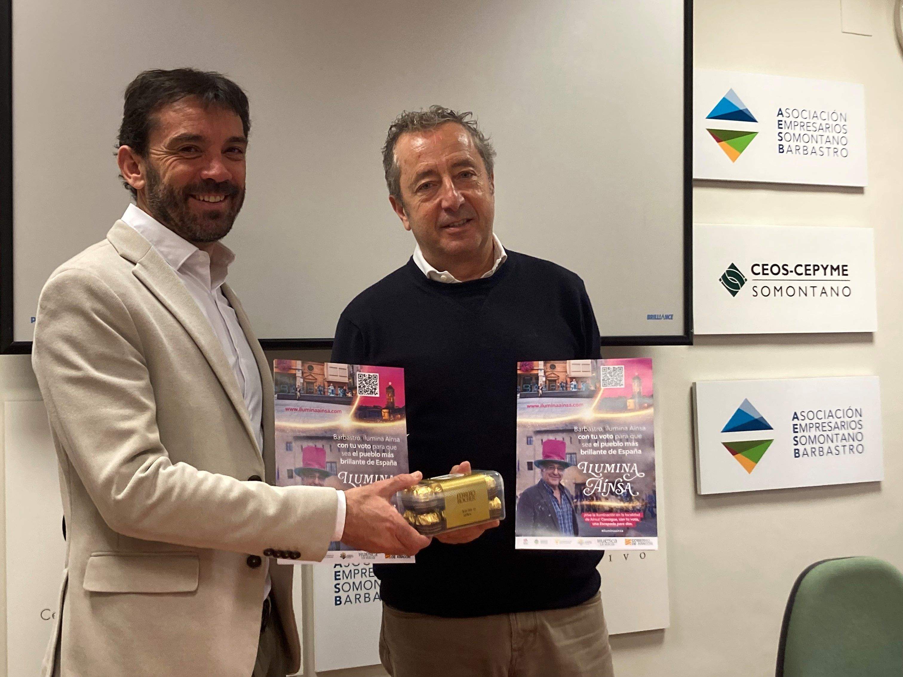 Enrique Pueyo entrega a Nacho Bernad unos bombones de Ferrero Rocher, y ambos sujetan el cartel de la campaña