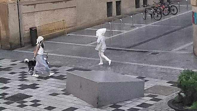 Dos viandantes se cubren la cabeza con lo que tienen a mano ante la tormenta Dos viandantes se cubren la cabeza con lo que tienen a mano ante la tormenta