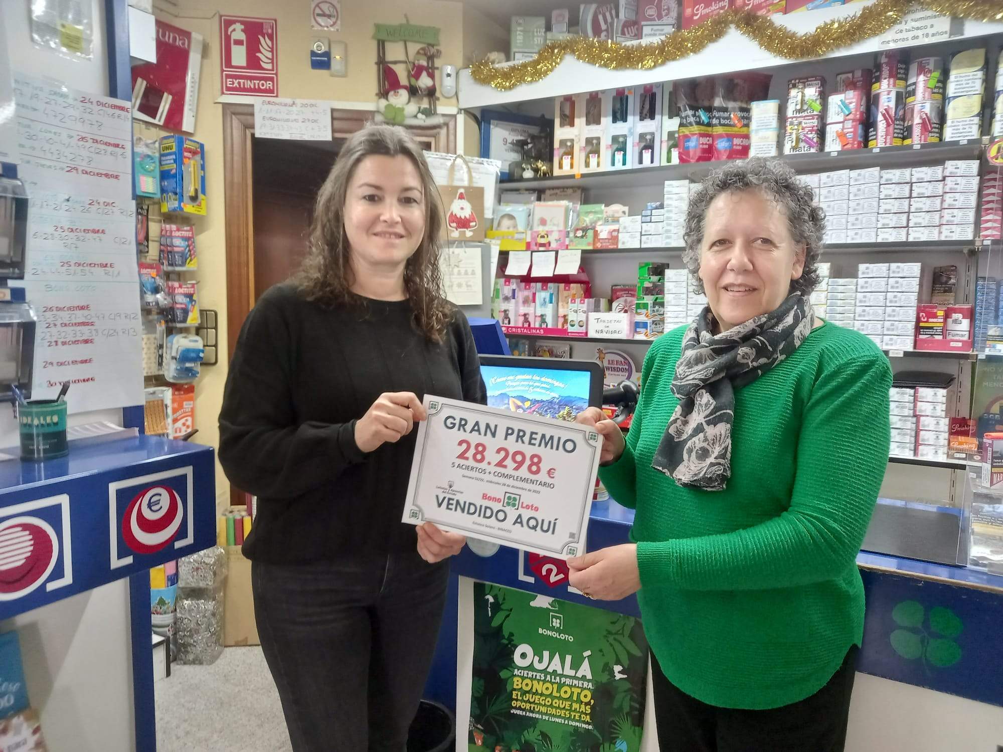 Dolores Solans, a la derecha, con el premio de una Bonoloto sellada en su establecimiento.