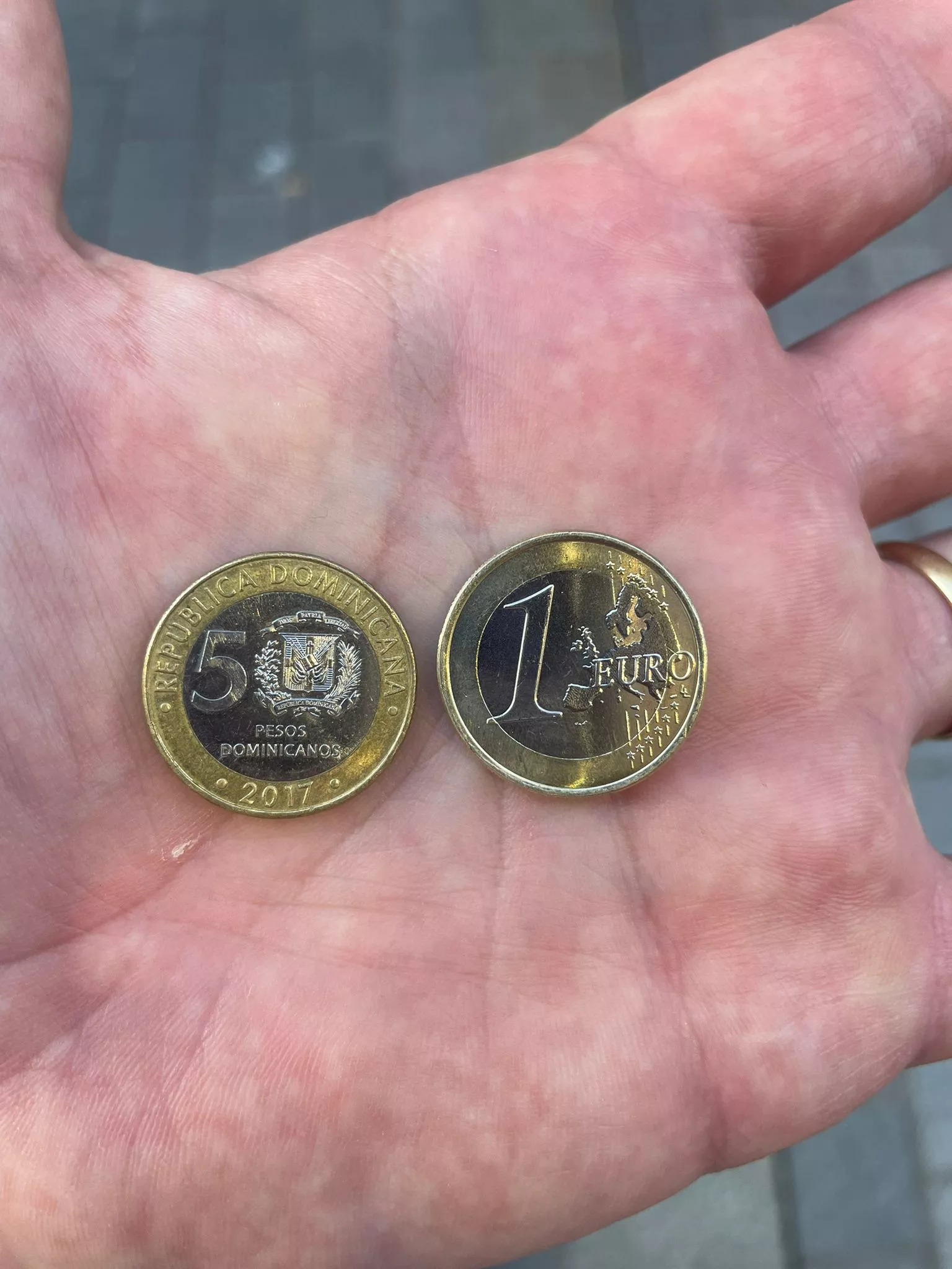Monedas de 5 pesos dominicanos y de euro en la mano de un oscense