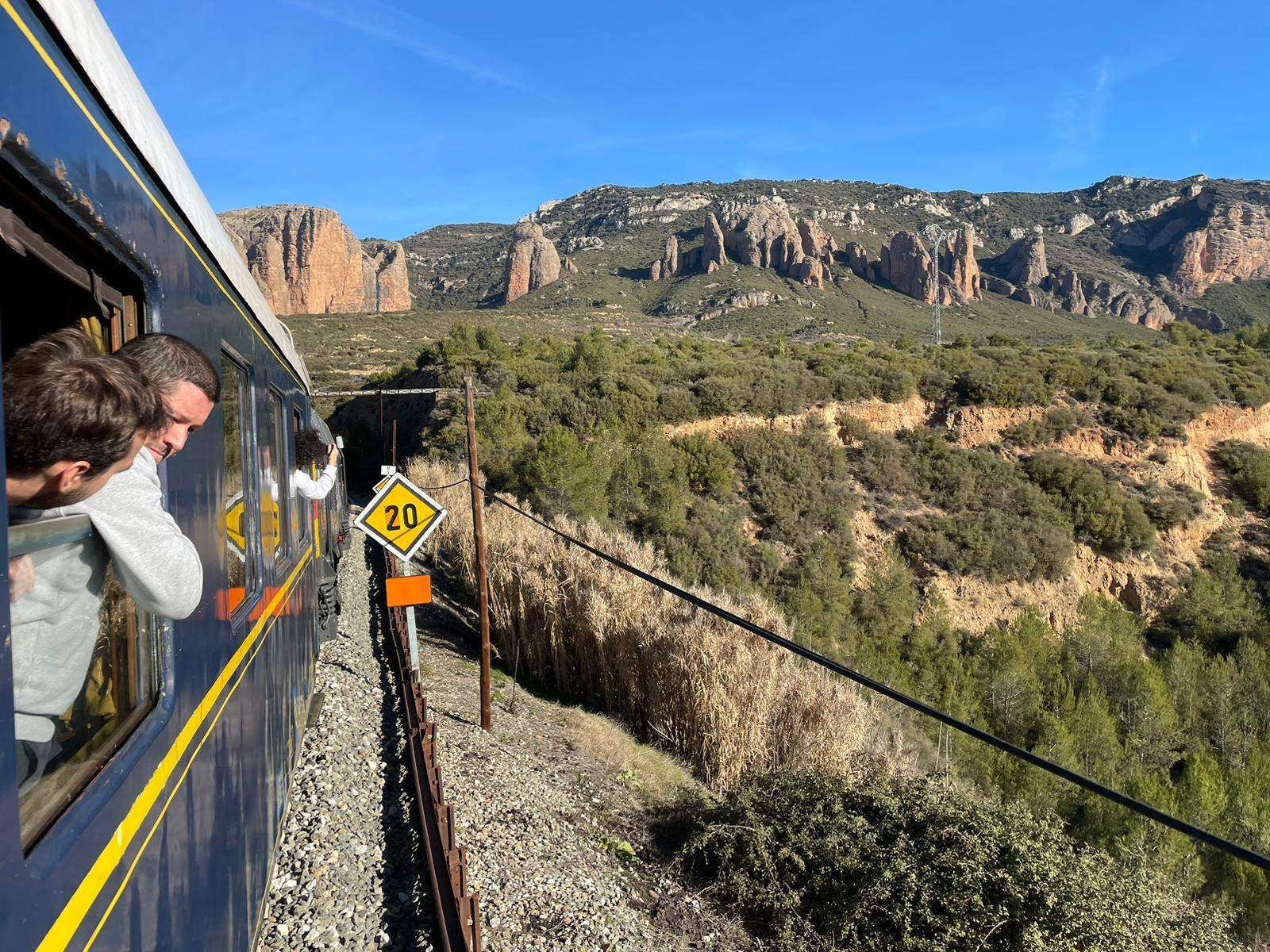 Viajeros del Tren Blanco disfrutan desde las ventanillas del paisaje, con los mallos del Riglos al fondo.