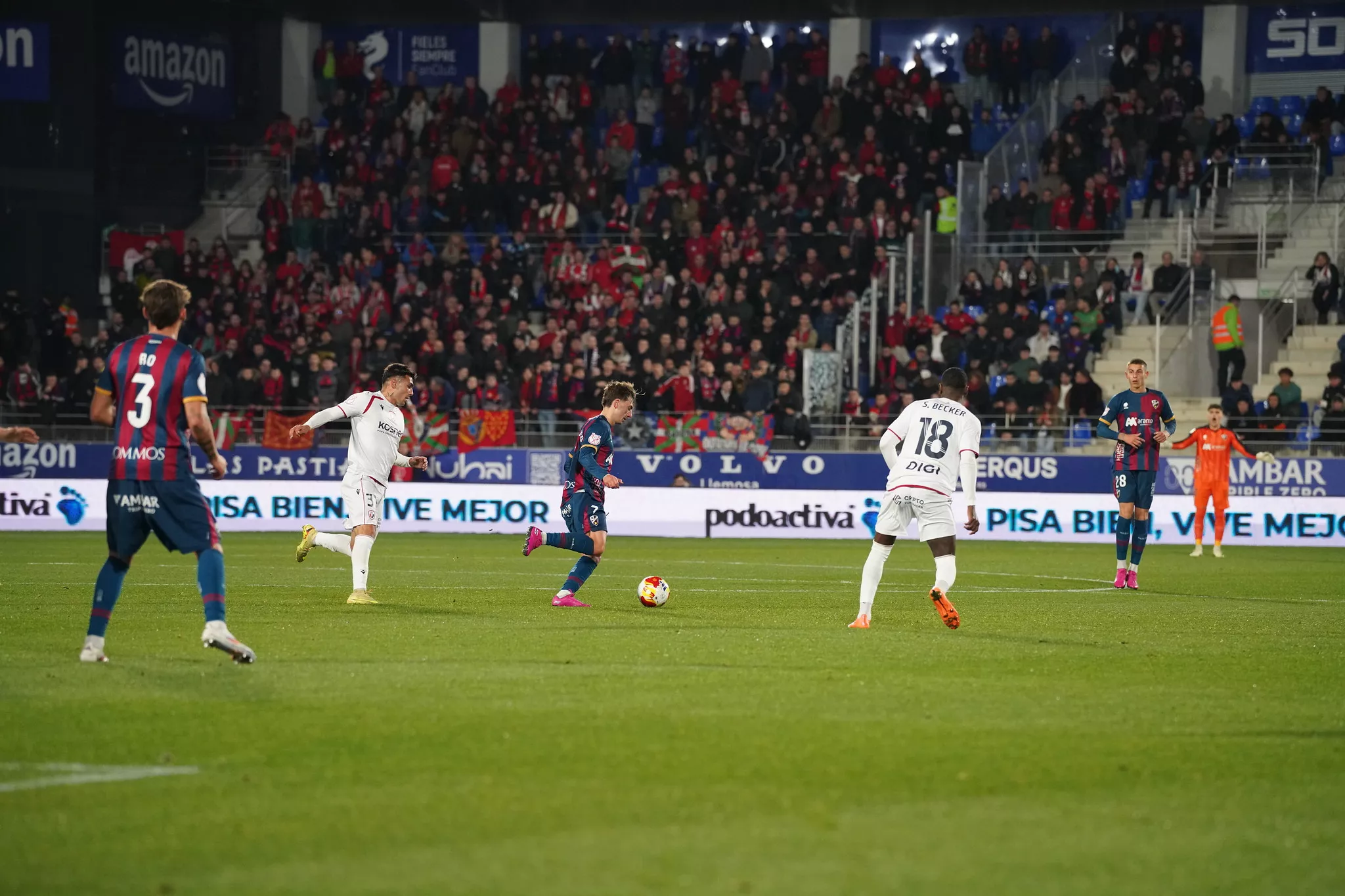Afición de Osasuna, al fondo, en el partido ante el Huesca en El Alcoraz. Rojillos y azulgranas: buena sintonía entre aficiones en el SD Huesca-Osasuna. Foto: Dani Vidal @fotomaniafut