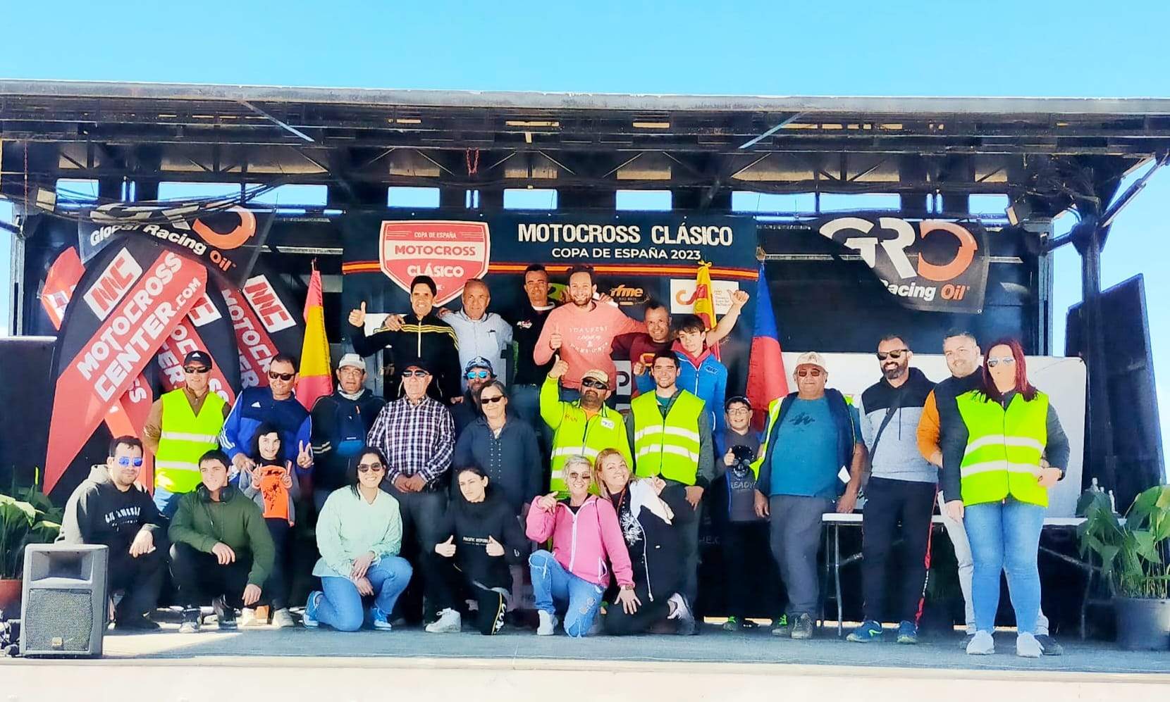 Voluntarios de la Copa de España de Motocross clásico 2023 posan en el podio junto a las autoridades.