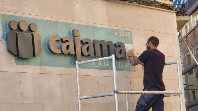Un operario destapa el letrero de Cajamar Un operario destapa el letrero de Cajamar
